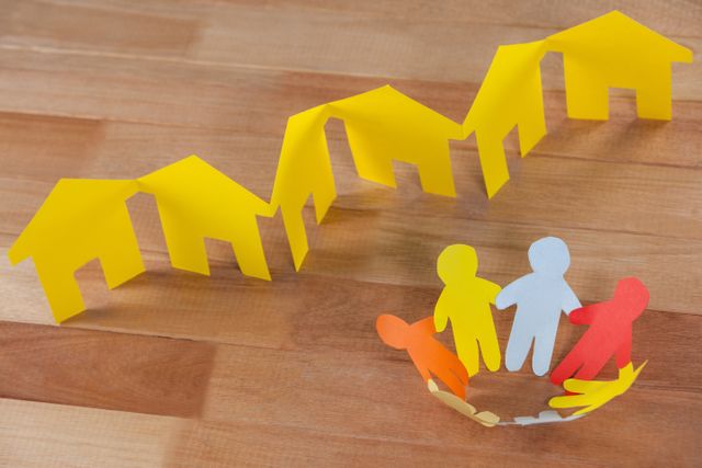 Conceptual image of paper cutout people standing in a circle against paper houses