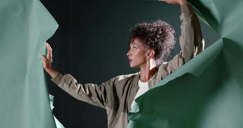 Woman tearing green paper backdrop revealing dramatic profile and dynamic studio lighting