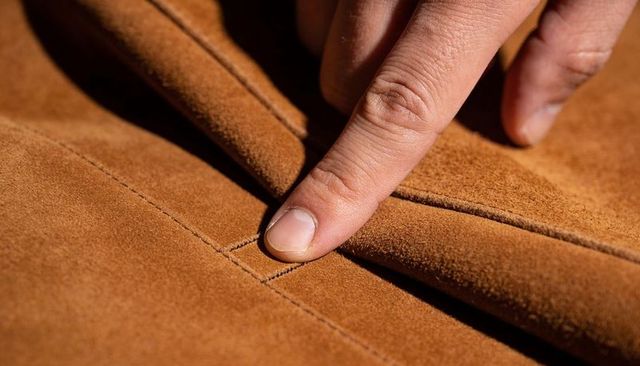 Finger tracing stitched seam on tan suede leather closeup highlighting texture