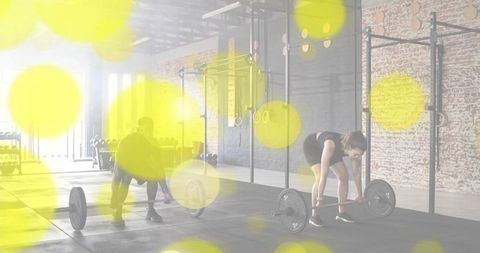 Partners preparing deadlifts in industrial crossfit gym with brick wall and yellow bokeh