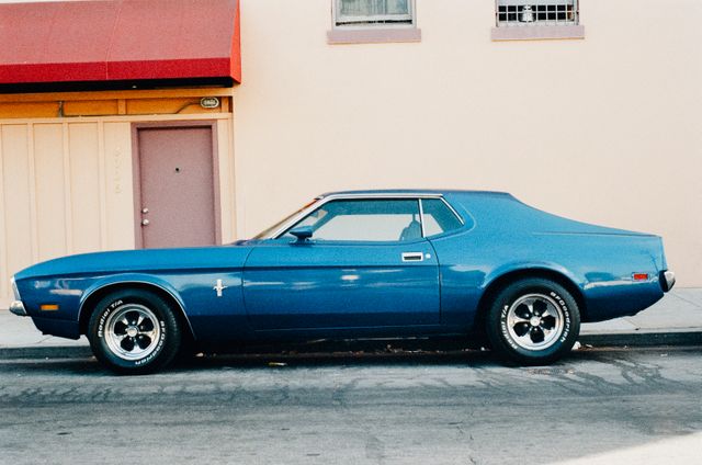 This image showcases a vintage blue muscle car parked on an urban street, evoking nostalgia and classic automotive beauty. Ideal for use in contexts related to vintage cars, urban culture, retro themes, car enthusiasts, and city living narratives.
