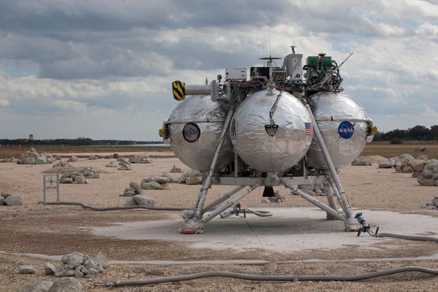 This depicts the NASA Project Morpheus prototype lander after a successful test landing in the ALHAT hazard field at Kennedy Space Center. It shows the lander with its silver spherical tanks and landing gear on a rocky surface. The sky is overcast, adding to the edge of a desolate, harsh environment. Useful for illustrating advanced space exploration technology, autonomous landing systems, and green propulsion research. Ideal for educational materials, technology magazines, aerospace articles, and presentations about NASA missions and development of exploration systems.