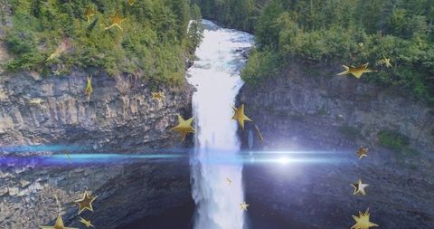 Plunging waterfall in forest canyon with golden stars and dramatic lens flare