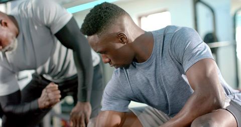 African american men strength training with personal trainer using dumbbells on bench