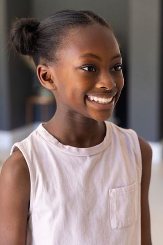 Smiling african pre-teen girl with double hair buns and stud earring in soft indoor light