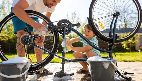 Father and son washing bike together in sunny backyard scrubbing soapy wheels and frame