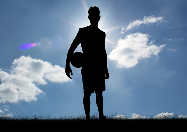 Silhouette of a football player standing outdoors with a football in hand against a bright sky with clouds. Ideal for use in sports promotions, fitness campaigns, motivational posters, and athletic event advertisements.