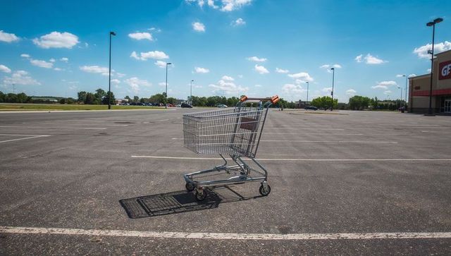 Shopping Cart Sitting Alone Casting Shadow on Expansive Sunny Parking Lot