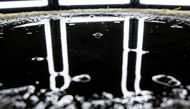 Vertical windows reflecting in shallow puddle on concrete with water droplets and bokeh