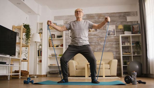 Senior man exercising with resistance band and dumbbells in cozy living room for strength