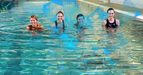 Four women smiling during aquatic fitness session standing chest-deep in indoor pool