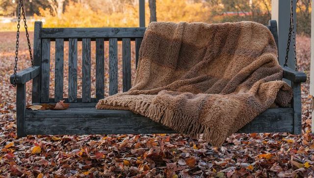 Cozy wooden swing bench with throw amidst autumn leaves