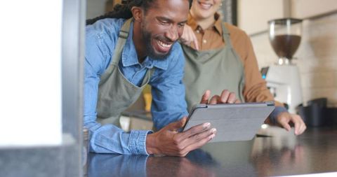 Smiling barista and coworker collaborating on tablet at modern coffee shop counter