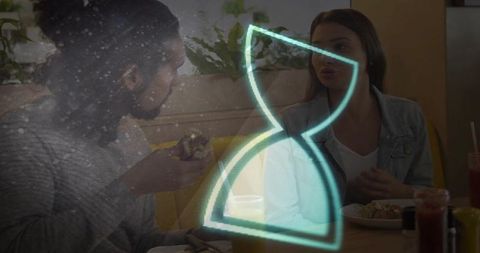 Couple Conversing and Sharing Meal in Cozy Cafe with Neon Hourglass Overlay
