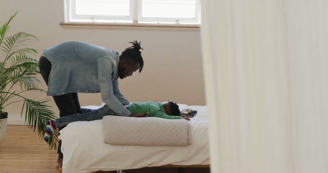 Father Dressing Child on Bed in Sunlit Room - Download Free Stock Images Pikwizard.com