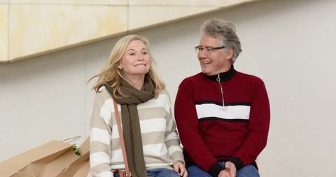Mature couple enjoying relaxed shopping break on outdoor bench in plaza