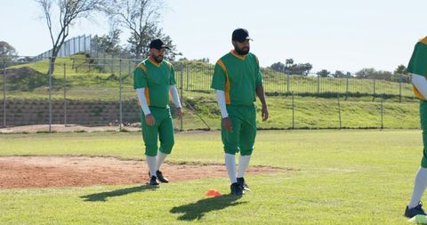 Baseball Teammates Walking on Field in Green and Yellow Uniforms During Training Drill