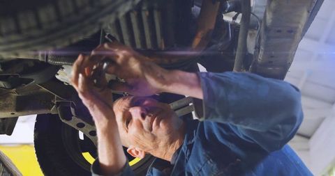 Skilled mechanic repairing vehicle undercarriage on lift in garage using wrench