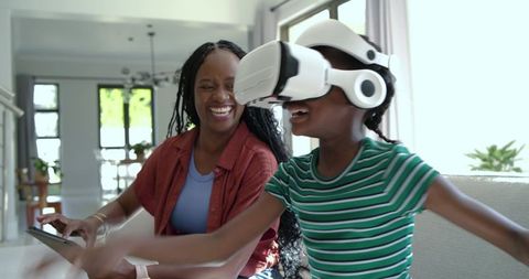 African American mother laughing with daughter exploring virtual reality at home