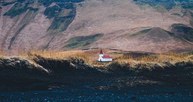 Photo showing a small, isolated church with a red roof situated in front of expansive mountains. Ideal for depicting concepts of solitude, peace, rural life, and scenic beauty. Perfect for travel blogs, nature websites, and promotional materials for outdoor retreats.