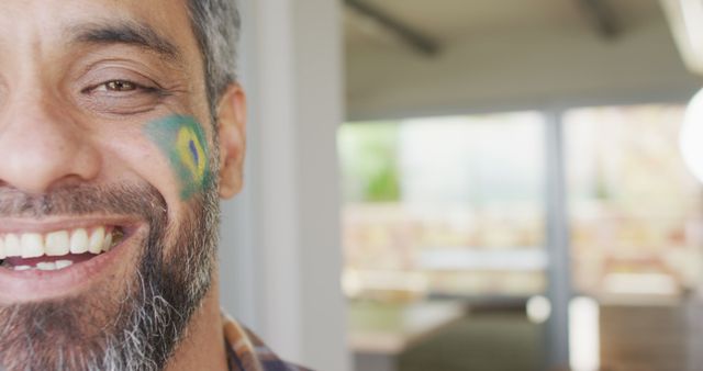 A close-up of a man with part of his face visible, showcasing a Brazilian flag face paint. He is smiling joyfully, likely indicating excitement and positivity. This image can be used for advertisements, blog posts, and articles related to sports events, Brazilian culture, or celebrations.