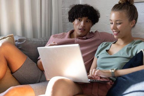 Young couple relaxing on sofa sharing laptop while browsing and planning at home
