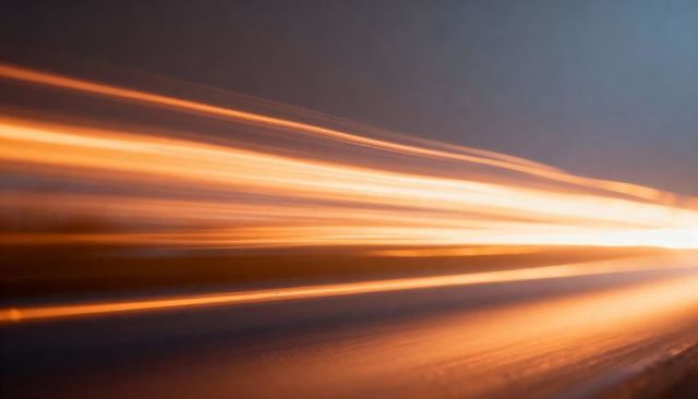 Streaming amber light streaks racing across reflective road toward vanishing point