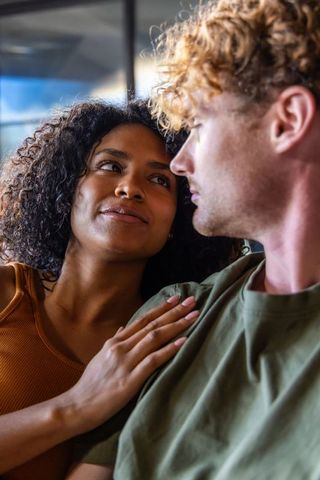Intimate diverse couple gazing, woman touching man's shoulder, warm natural window light