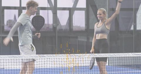 Young couple playing padel on indoor blue court celebrating winning point together