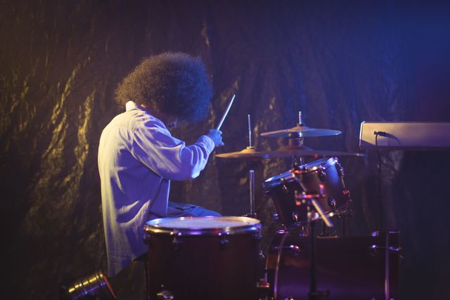 Side view of male drummer with frizzy hair playing drum kit in nightclub