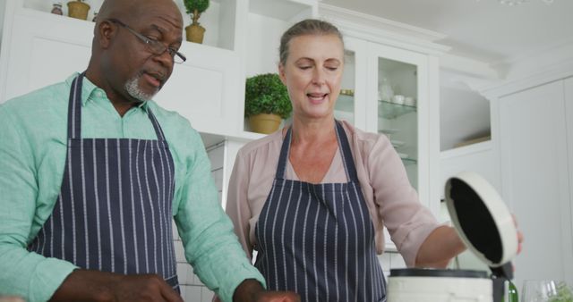 Smiling Senior Diverse Couple Cooking in Kitchen Wearing Blue Aprons - Download Free Stock Images Pikwizard.com