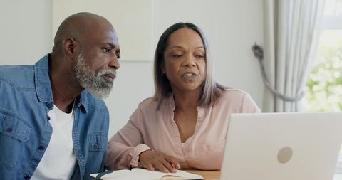 Mature couple reviewing finances on laptop and notebook at home, planning retirement