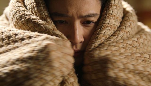 Asian woman wrapping in woven blanket embracing warmth cozy closeup portrait