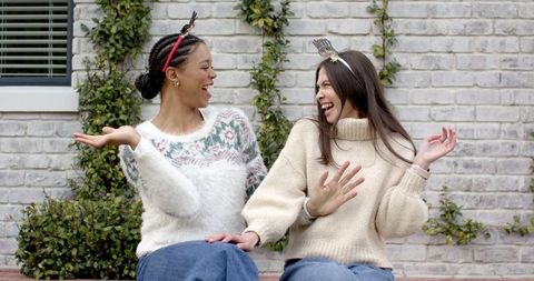Friends Laughing on Courtyard Bench Wearing Cozy Knit Sweaters and Jeans