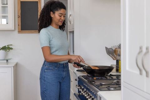 African American Woman Cooking with Wok on Gas Stove in Modern Kitchen