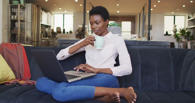 Young Woman Working from Home with Laptop and sipping Coffee on Sofa - Download Free Stock Images Pikwizard.com