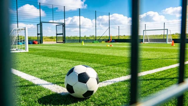 Black-and-white soccer ball sitting on corner line of artificial turf with goals and training cones