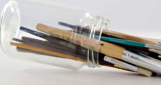 Assorted paintbrushes in a transparent glass jar lying on its side. Ideal for art supply websites, creative project promotions, or advertisements for painting workshops.