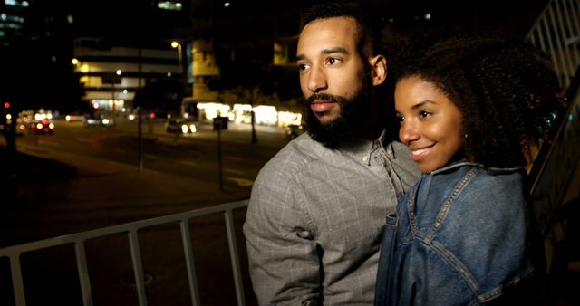 Romantic diverse couple smiling and embracing in city street at night. City living, romance, love, relationship, free time and lifestyle, unaltered.