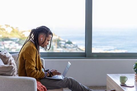 African american man working remotely on laptop by ocean-view window