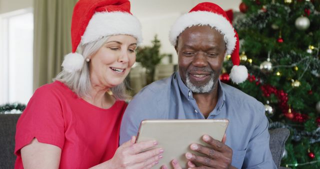Happy senior diverse couple using tablet at christmas. Spending quality time at christmas and retirement concept.
