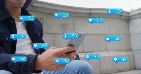 Young man sitting on plaza steps checking smartphone with social notification bubbles