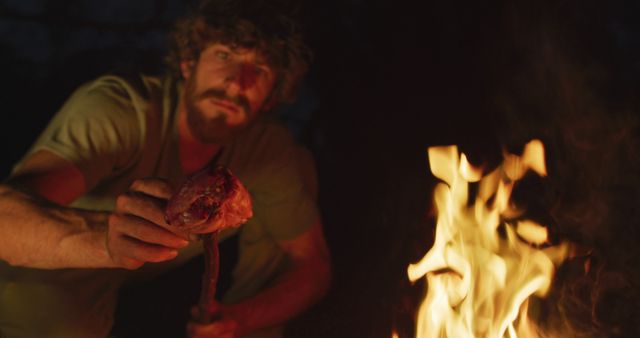 Smiling bearded caucasian male survivalist in wilderness, cooking meat on stick in evening campfire - Download Free Stock Photos Pikwizard.com