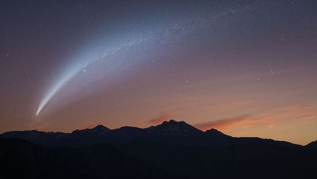 Comet arcing over mountain peaks with sweeping luminous tail and starry twilight sky