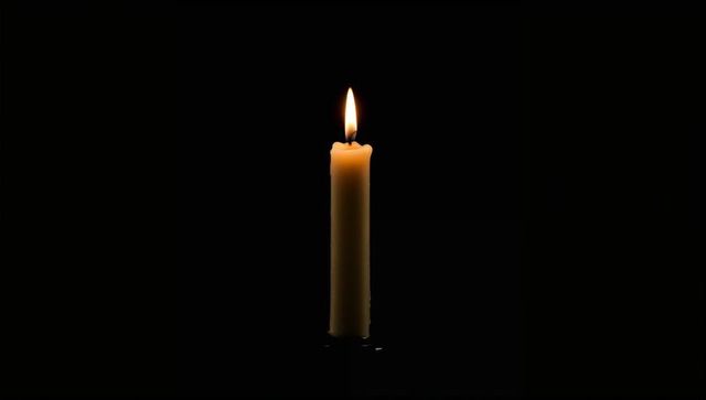 Solitary taper candle burning with teardrop flame on dark background, minimal candlelight