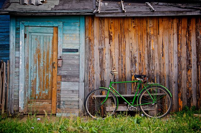 Vintage green bicycle leaning against worn rustic wooden shed. Ideal for themes of nostalgia, rural lifestyle, outdoor scenes, and retro aesthetics. Perfect for articles, blogs, websites, vintage-themed projects, and posters.
