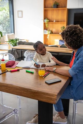 Mother guiding daughter at home with creative writing activity