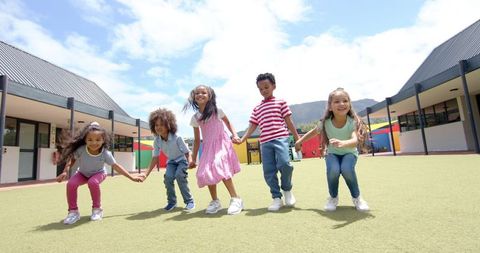 Diverse Children Joyfully Jumping Together Outdoors at School