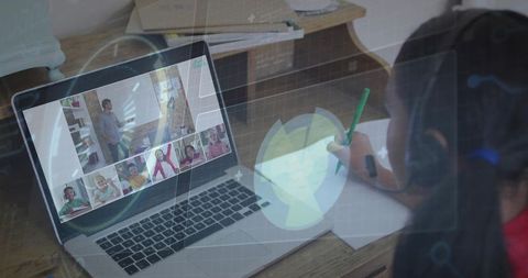 Child learning online at laptop wearing headphones writing notes during virtual classroom