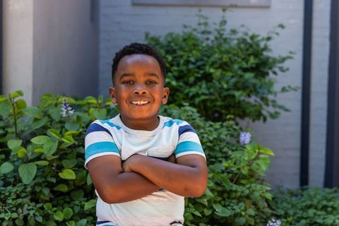 African american boy smiling and standing with arms crossed in sunny courtyard garden
